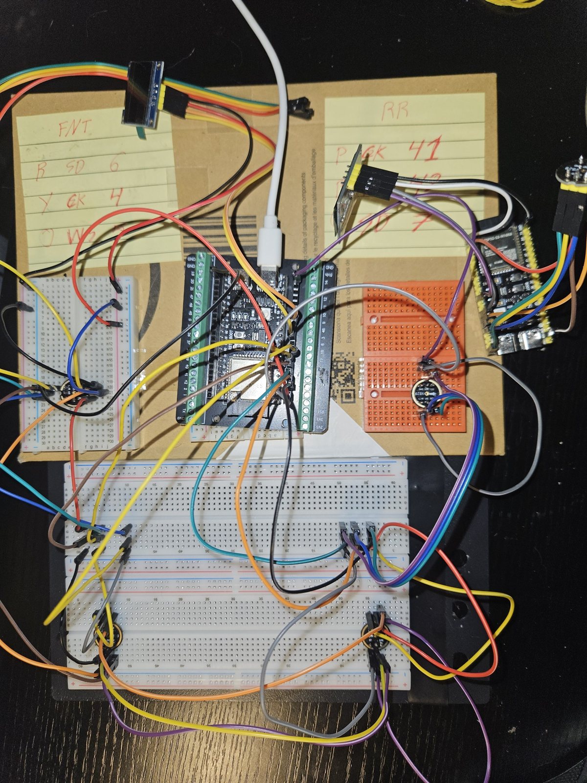 Breadboards on cardboard wired to an ESP32-S3 devkit, with hand-written GPIO notes on yellow paper