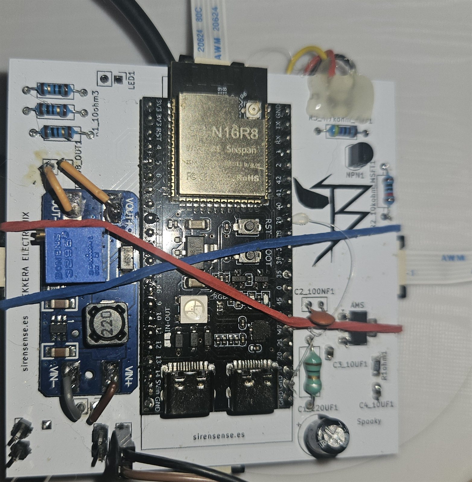 A white board with an ESP32-S3 module and passives under test, with test leads clipped on